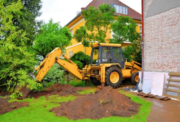 Excavator digging up the back lawn of a residential property to access underground drain, sewer or stormwater pipes.